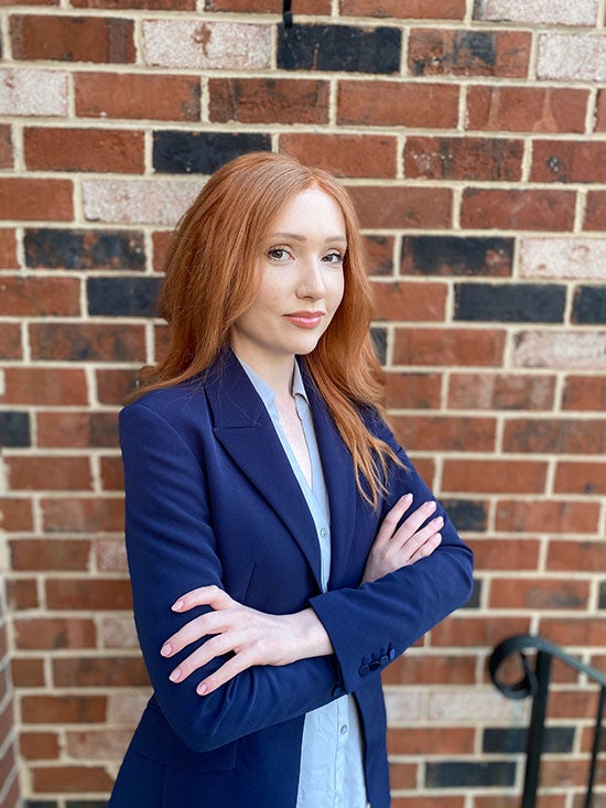 Mary Barthelson standing in front of a brick wall with her arms crossed.