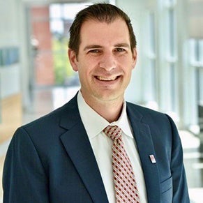 The late Kevin Fendl, Schar School PhD in Public Policy alumni, in a suit, tie, and white shirt smiling at the camera.