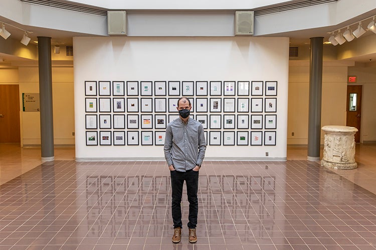 Michael McDermott is wearing a mask and standing in front of part of his exhibit of found images and text
