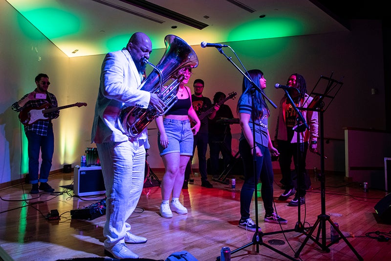 Dox Nix wears a white suit and plays the tub on stage with members of the Green Machine