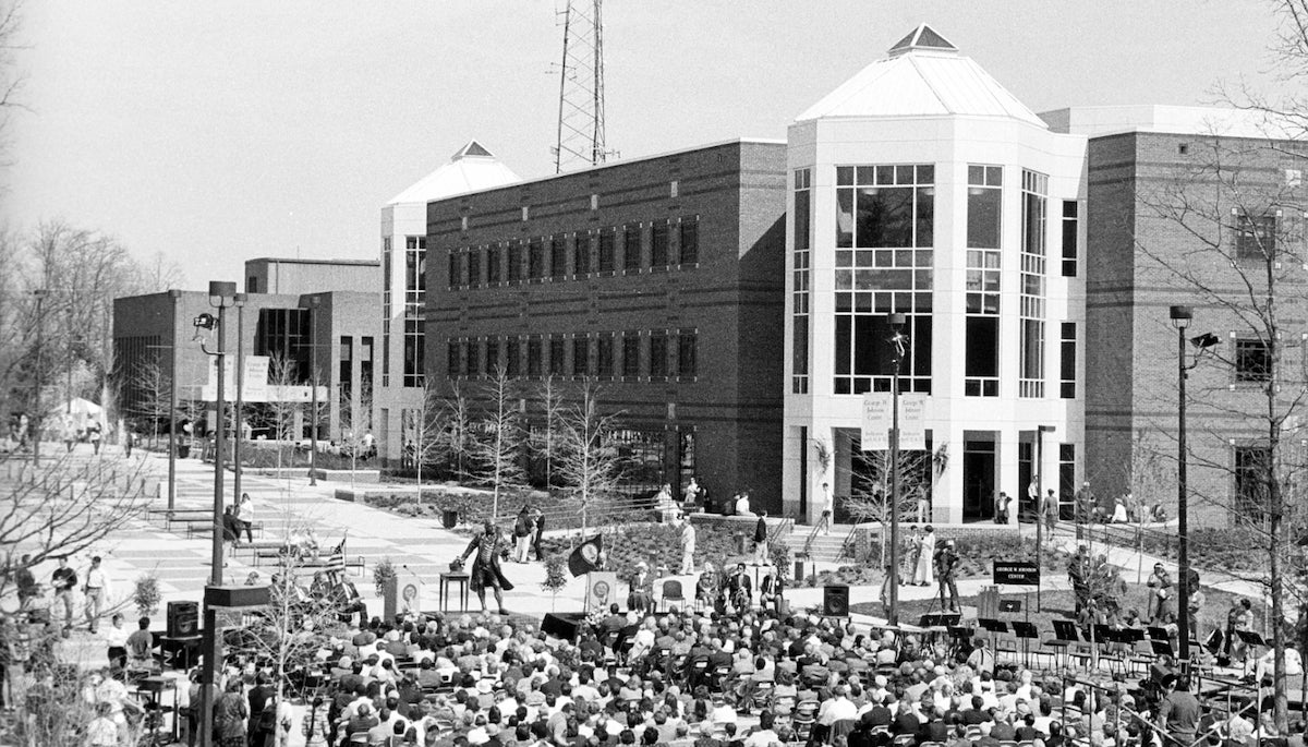 black and white photo of people sitting on folding chair outside of a brick building