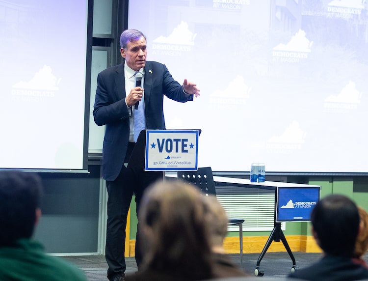 man in suit talking to students from stage