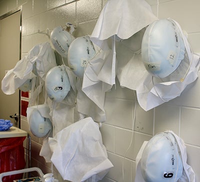 White helmets hang on a white cinderblock wall.
