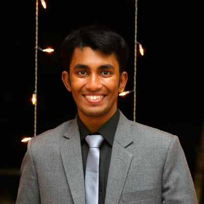 Majidur Rahman, IST PhD student at Mason, wears a gray suit, dark shirt, and light tie in front of a lit background.