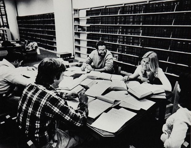Students smile and laugh as they sit at a library table to study.
