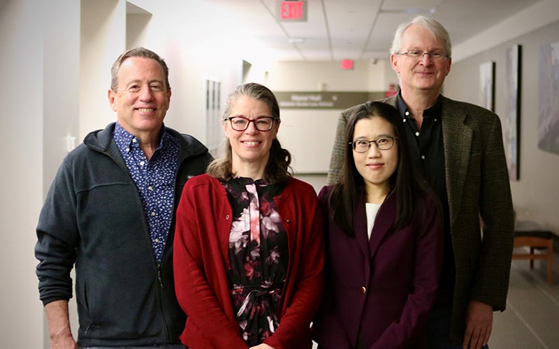 Four people standing in a hallway smile for the camera.