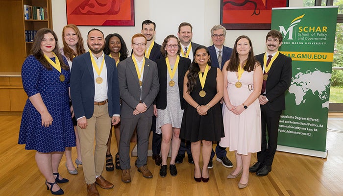 A group of well-dressed young people wearing yellow ribbons with gold medals smile for the camera.