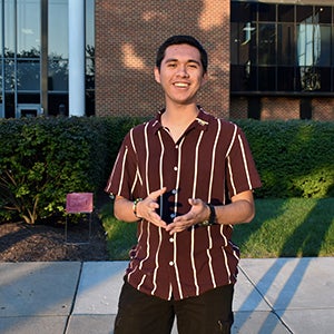 A young man in a brown shirt with white stripes smiles broadly.