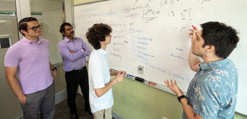 four men work on math problems on a whiteboard