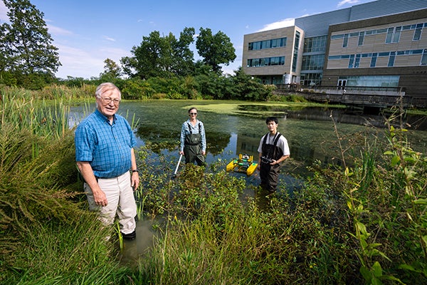 Jones, McCue, and Li pose in the pond with the surface water vehicle. 