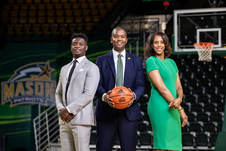 Tony Skinn, Marvin Lewis holding a basketball, and Vanessa Blair-Lewis on the EagleBank Arena basketball court