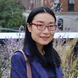 A woman with long dark hair wearing red glasses smiles at the camera.