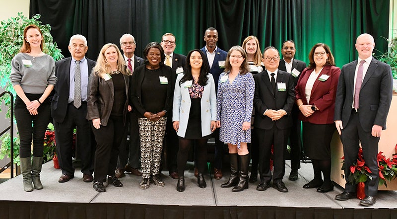A group of nicely dressed people stand in front of a black backdrop on a stage.