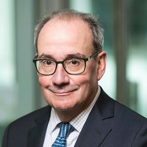 A man in a dark jacket and eyeglasses smiles at the camera.