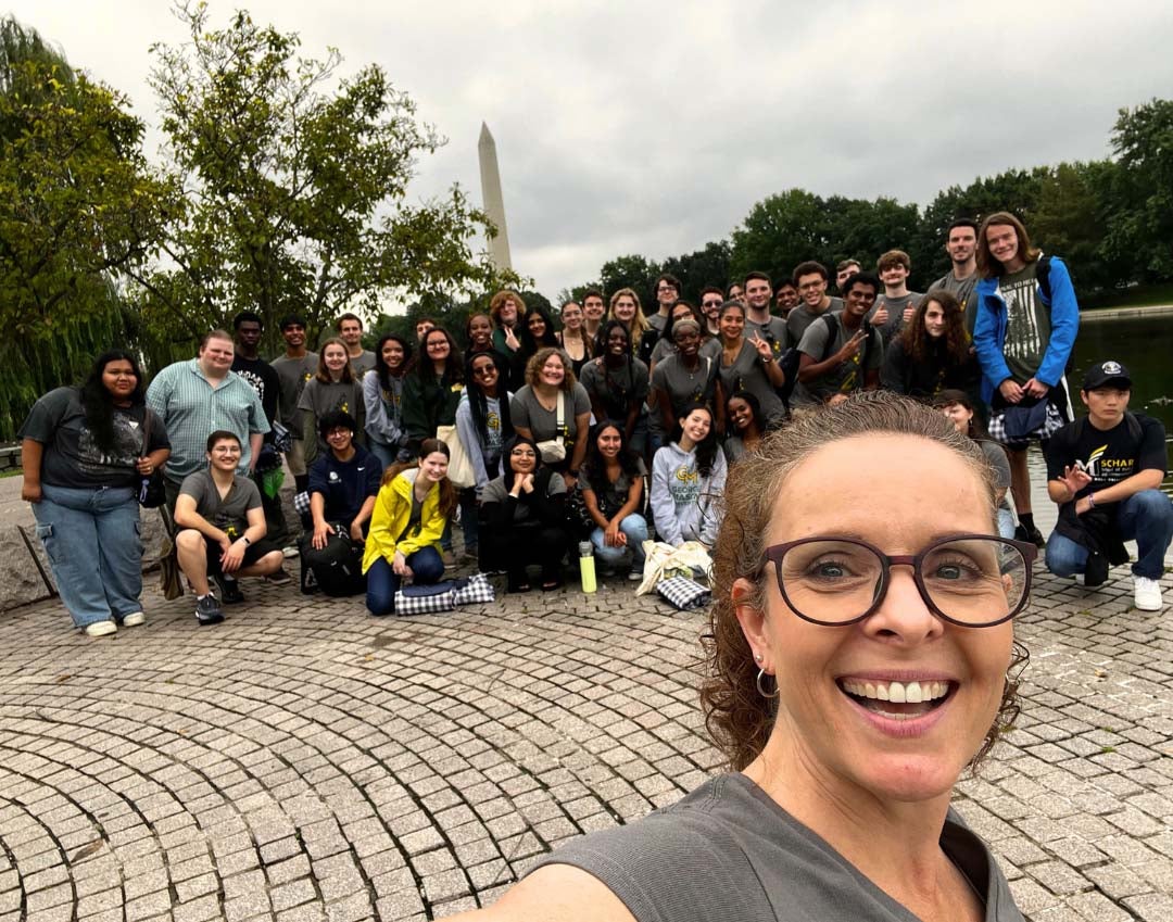 A woman in the foreground takes a selfie with a large group of students near the Washington Monument.