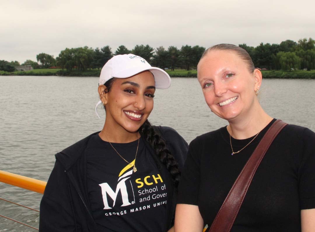 Two women, one wearing a baseball cap, smile while on a boat ride.