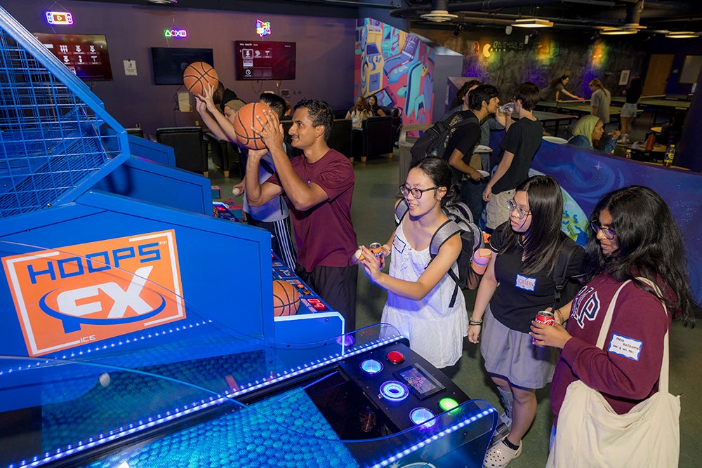 Five students line up to play a basketball arcade game.