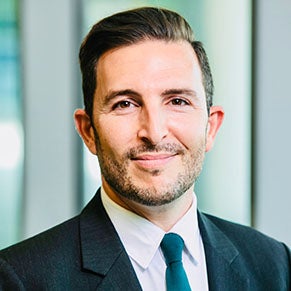 A man with a beard wearing a jacket and tie smiles for the camera.