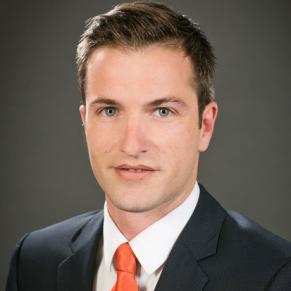 A young man in a dark jacket and red tie poses for the camera.