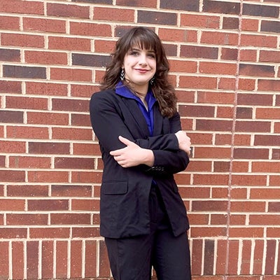 A young woman in black leans against a brick wall.
