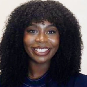 A woman in a blue shirt stands and smiles