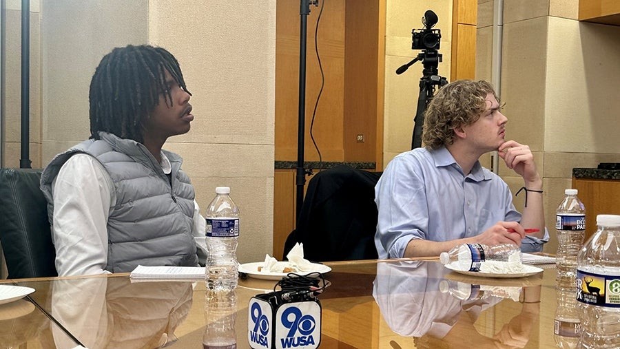 Two people sit at a table and stare off camera at something.