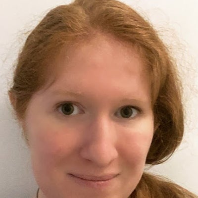 A woman with long red hair stands inside and smiles