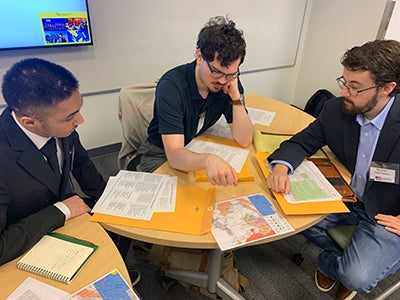 Three graduate students at a table reviewing maps and policy documents during a CSPS crisis simulation on the South China Sea.