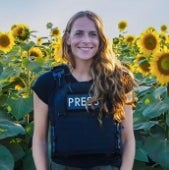 A woman with a Press vest stands outside in front of some sunflowers and smiles