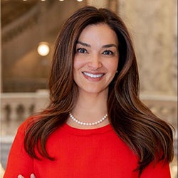 A woman with long dark hair and wearing a red top smiles at the camera.