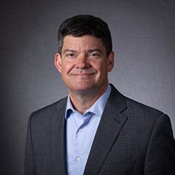 A man in a dark jacket and light shirt gazes at the camera.