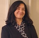Headshot of Hina Kazmi smiling at the camera, wearing a dark blazer and light blouse, against a neutral background.