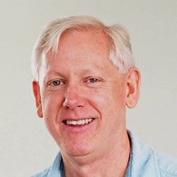 Headshot of Greg Brandon in business attire, smiling against a neutral or studio background.