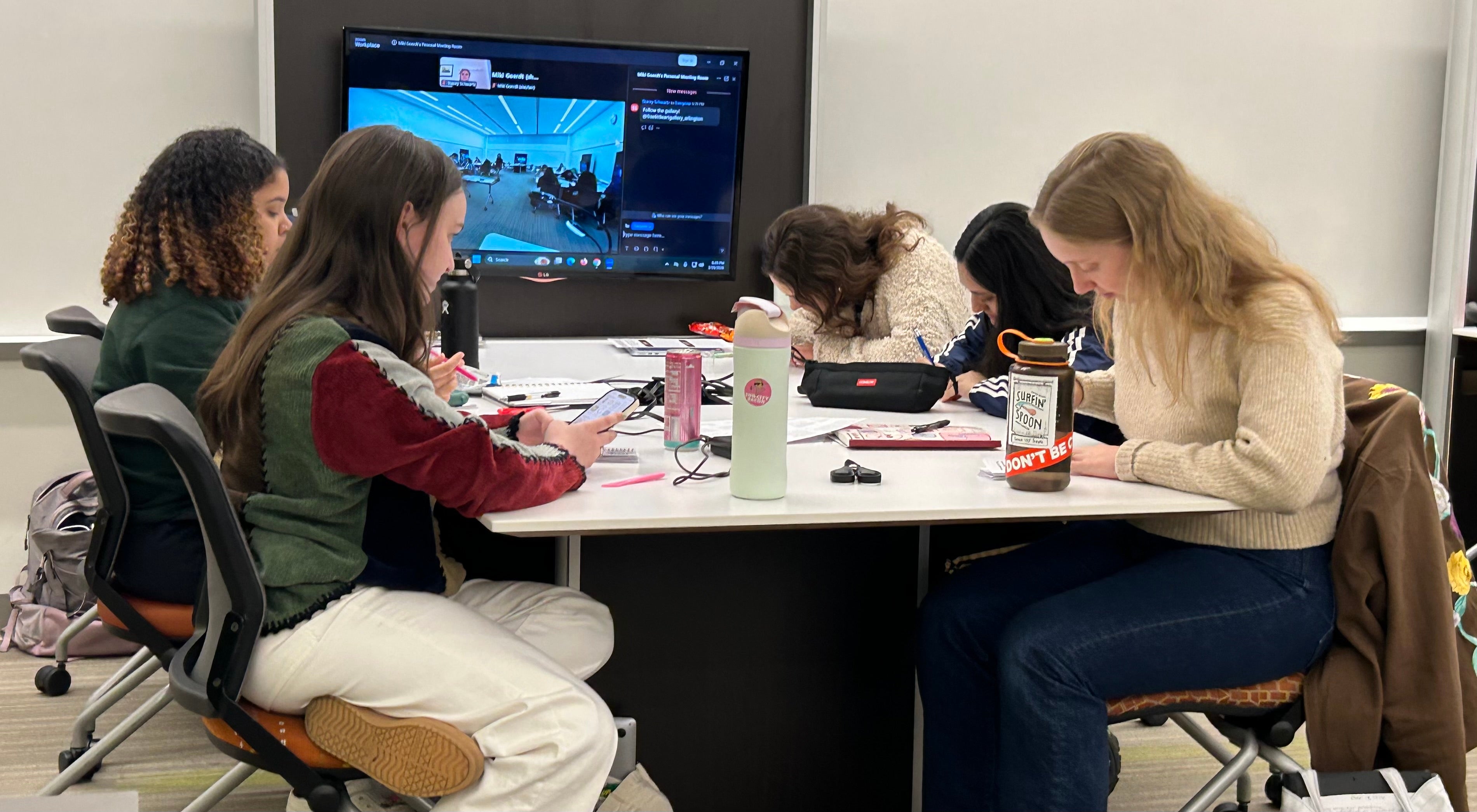 5 students sitting around a white table and drawing their designs for their mini prints for the Free Little Art Gallery.