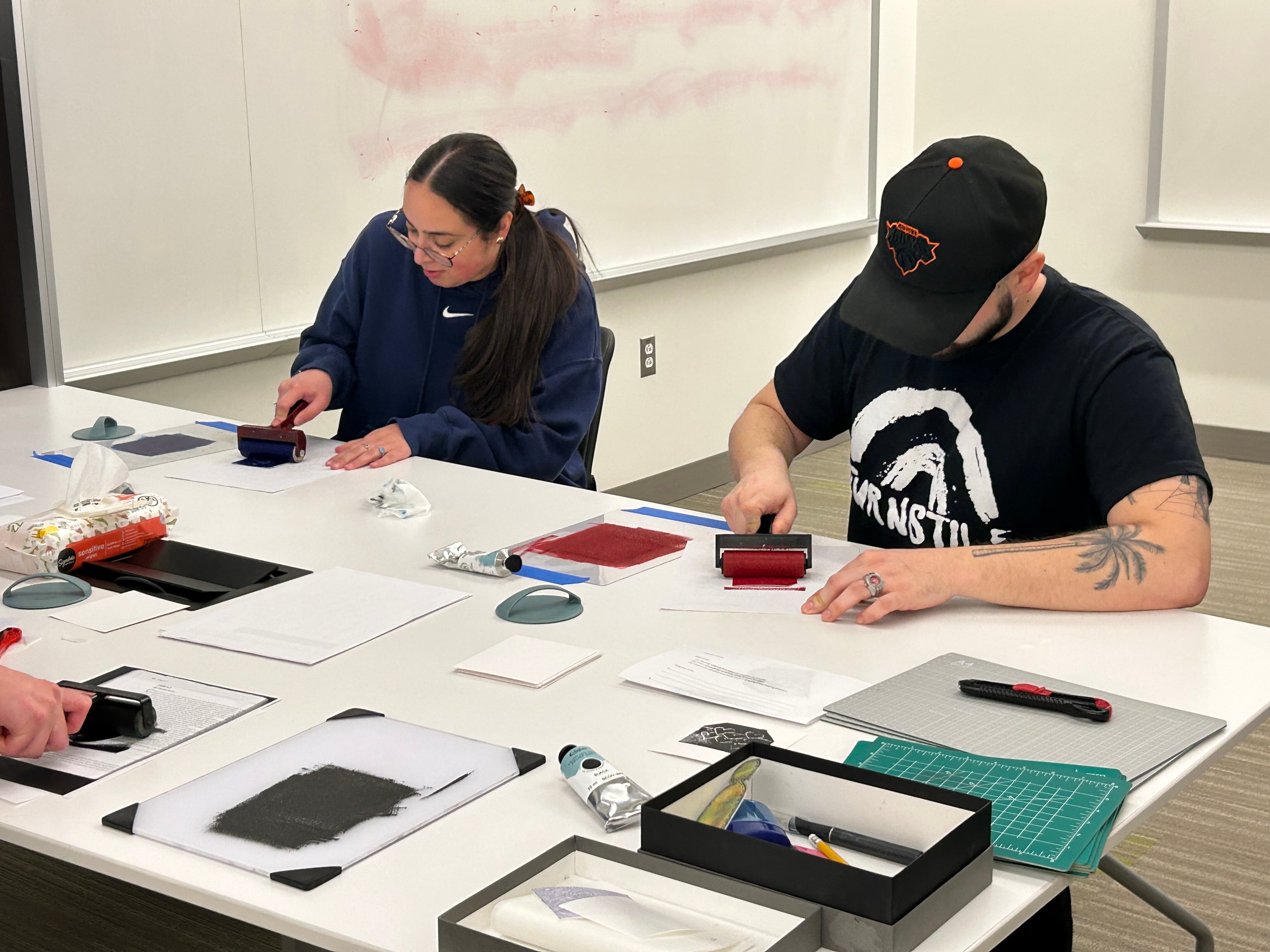 Two students sitting and rolling ink on their mini prints.