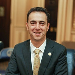Headshot of Virginia Delegate Marcus Simon in a suit and tie, smiling against a neutral background.