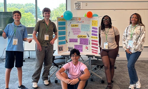 Students stand in front of a poster presentation showcasing their creative work