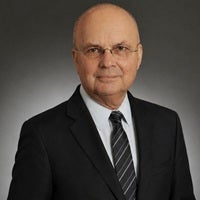 Professional headshot of General Michael Hayden wearing a dark suit, white shirt, and striped tie against a gray background.