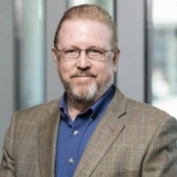 Professional headshot of Larry Pfeiffer wearing a tan blazer and blue shirt, standing in front of a blurred office background.