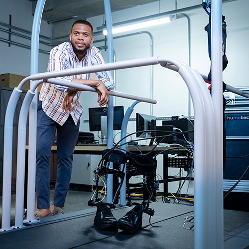 A man stands by a treadmill with lower limb prosthetics balanced on the treadmill.