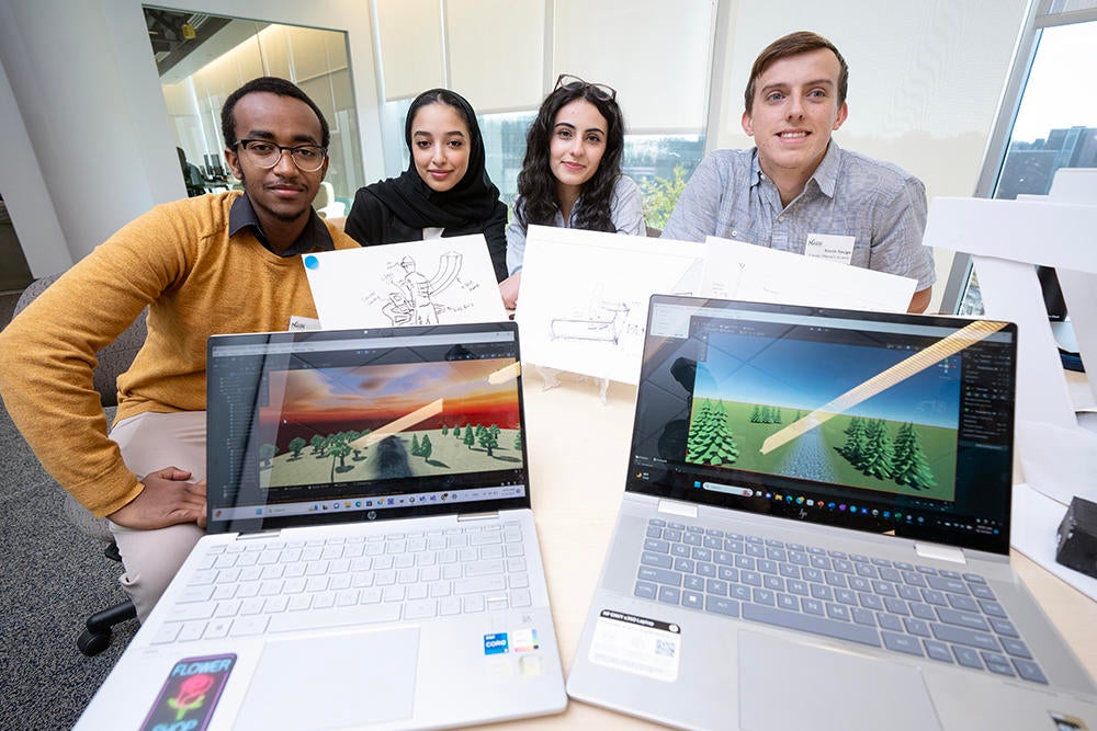 Students sit behind two laptops and sketches showcasing their work