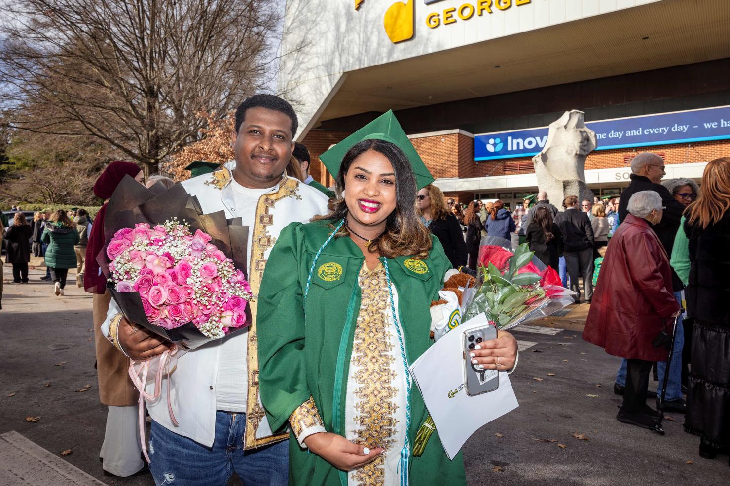 Graduate smiles and holds flowers from a loved one outside the arena