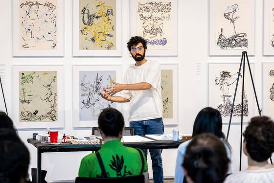 bearded man standing before artwork talking to audience