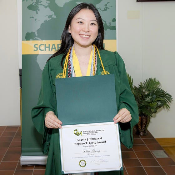 A woman in a green gown holds a certificate and smiles.