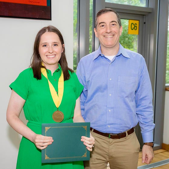 A woman in a green dress wearing a medal stands next to a smiling man in a blue shirt.