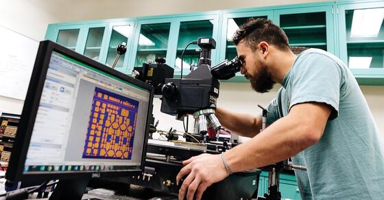 A George Mason physics PhD student uses a microscope to probe nanoelectronic devices.