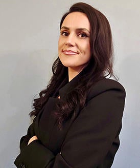 A woman with long dark hair looks at the camera with her arms folded.