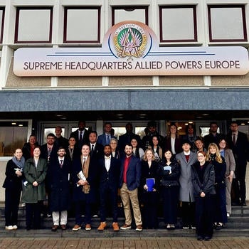A group of people stand under a sign that says Supreme Headquarters Allied Powers Europe.