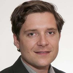 A man with brown hair and brown eyes smiles at the camera.