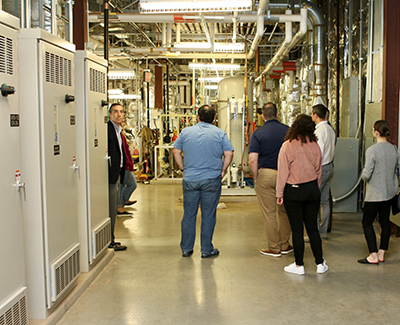 A group of people with their backs to the camera gaze at a room of pipes and lights.